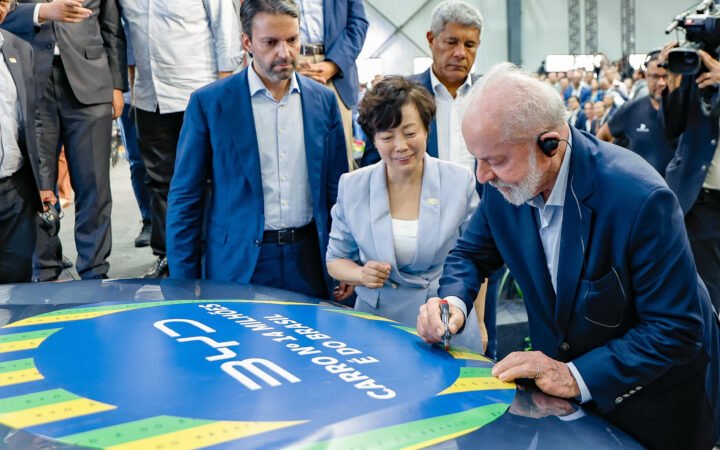 Lula assina com caneta o capô de um carro da BYD durante a inauguração da fábrica em Camaçari, Bahia, ao lado de uma executiva da empresa