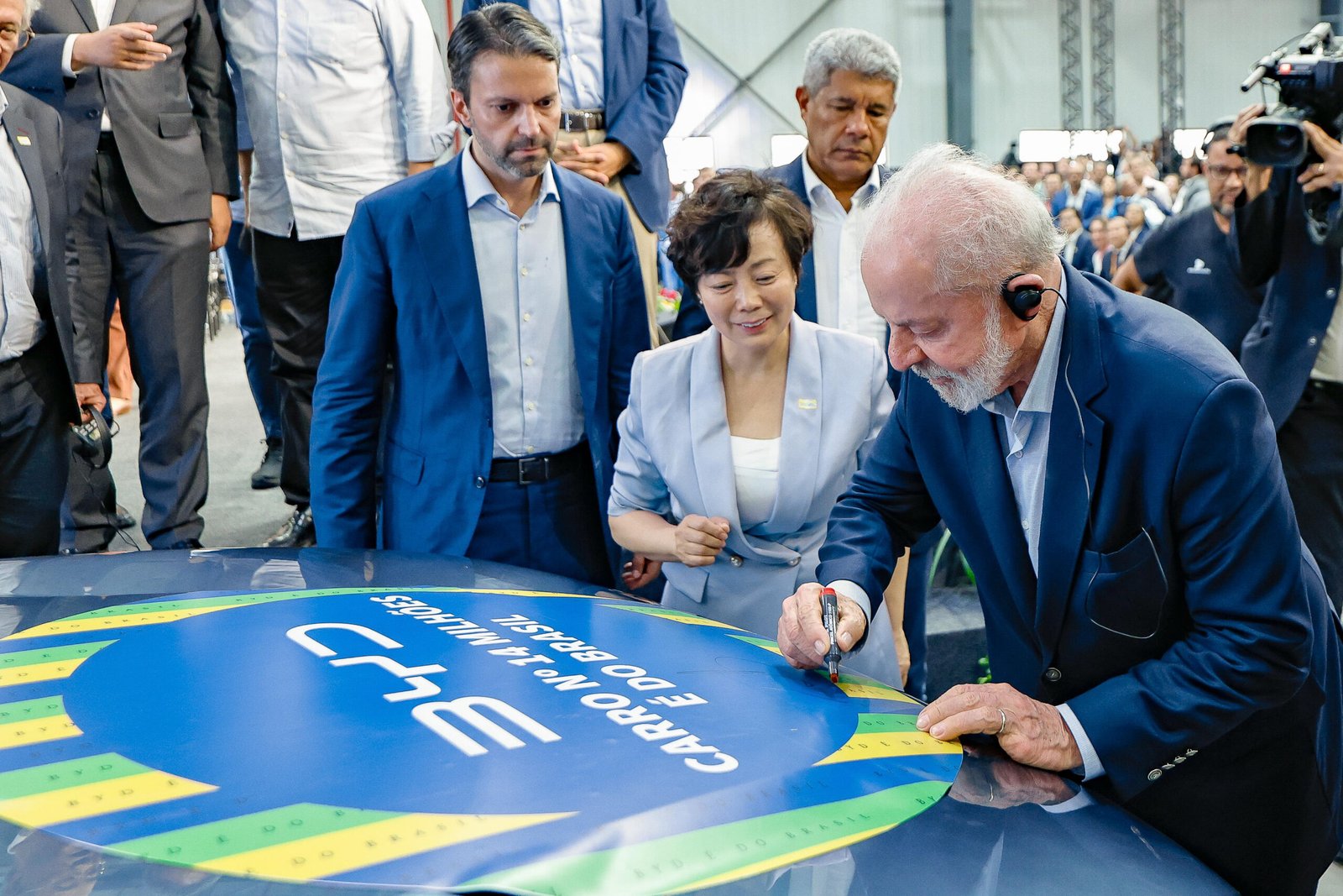 Lula assina com caneta o capô de um carro da BYD durante a inauguração da fábrica em Camaçari, Bahia, ao lado de uma executiva da empresa
