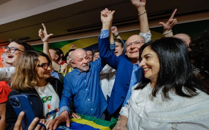 O presidente Lula, de braços erguidos, cercado de apoiadores na noite da reeleição