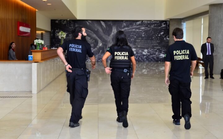 Três agentes da Polícia Federal caminham por um saguão