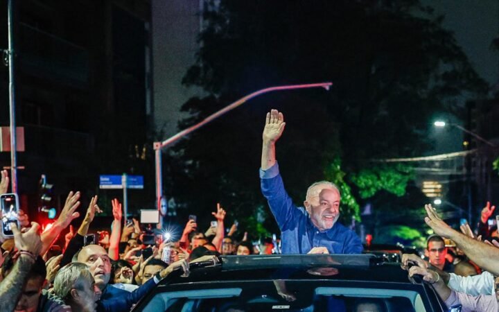 O presidente Lula acena sobre um carro para uma multidão à noite