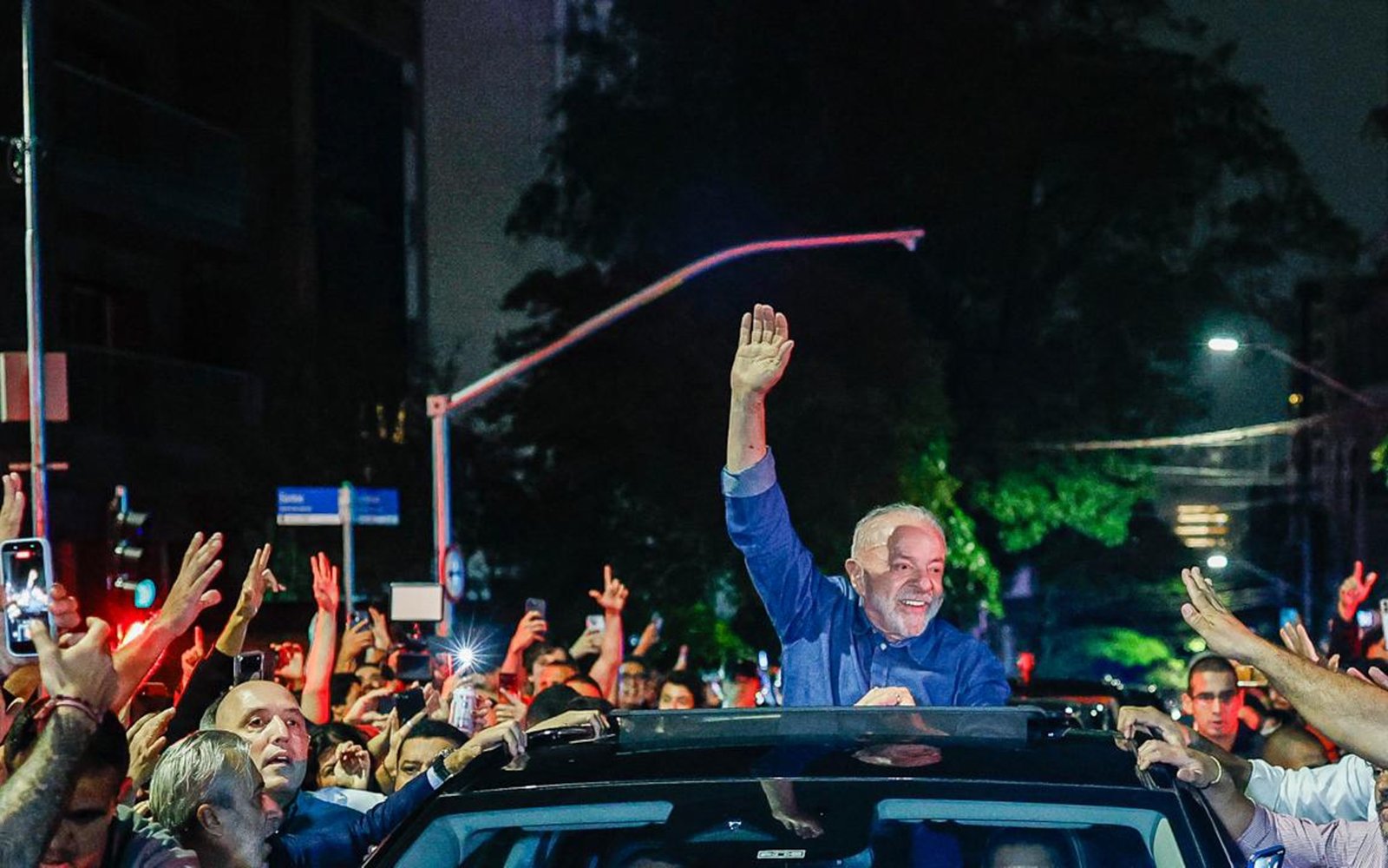 O presidente Lula acena sobre um carro para uma multidão à noite