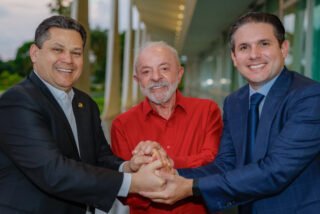 Davi Alcolumbre, Lula e Hugo Motta de mãos dadas, sorrindo, em corredor do Palácio da Alvorada