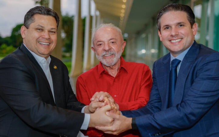 Davi Alcolumbre, Lula e Hugo Motta de mãos dadas, sorrindo, em corredor do Palácio da Alvorada