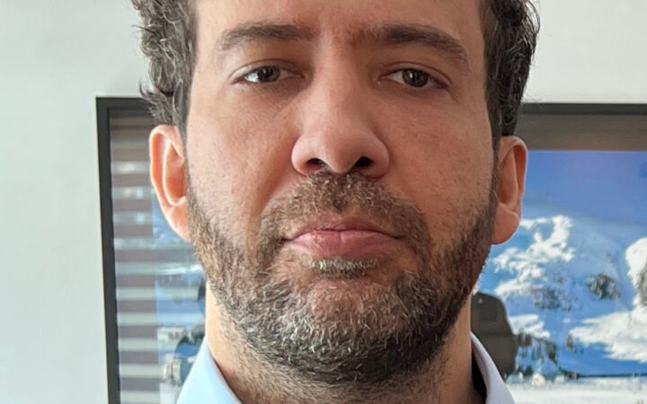 Retrato do deputado federal André Janones, de barba, camisa azul e suéter escuro