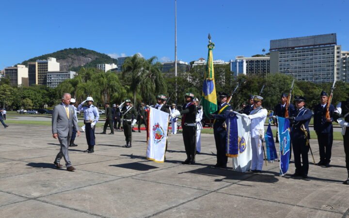 O ministro da Defesa, José Múcio Monteiro, de terno cinza, caminha diante de militares perfilados com bandeiras durante a cerimônia do Dia da Vitória, no Rio de Janeiro.