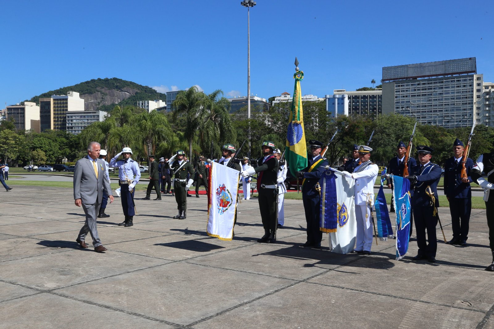 O ministro da Defesa, José Múcio Monteiro, de terno cinza, caminha diante de militares perfilados com bandeiras durante a cerimônia do Dia da Vitória, no Rio de Janeiro.
