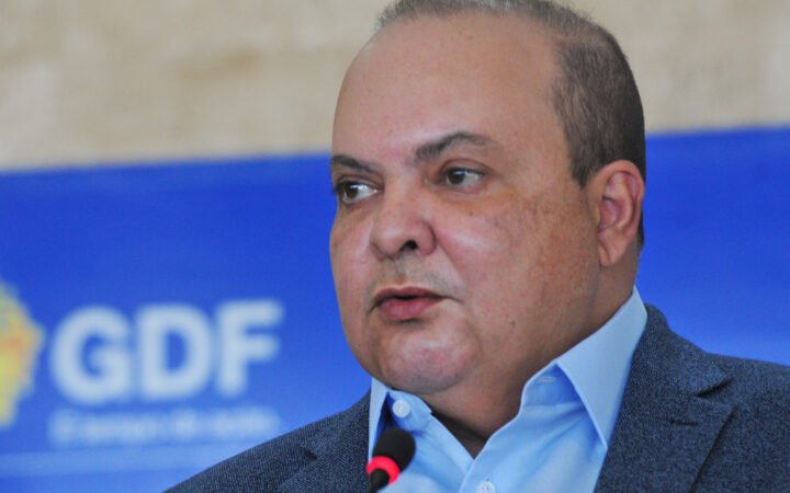 Ibaneis Rocha, de blazer cinza, falando ao microfone diante de um painel azul do governo do Distrito Federal