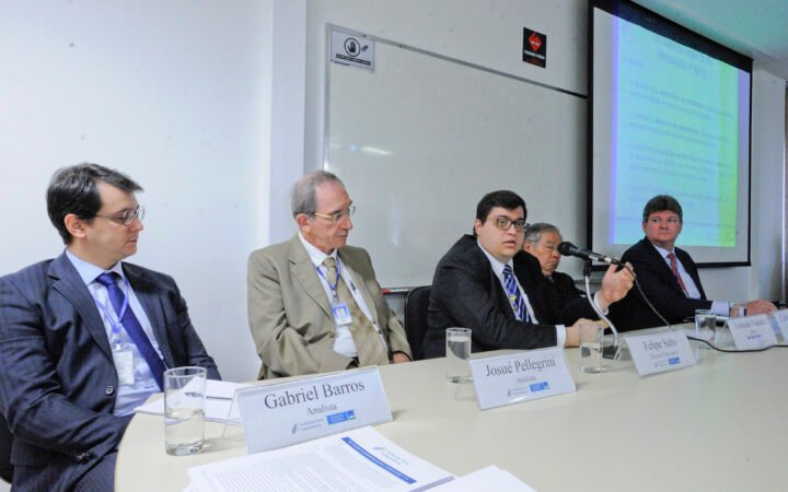 Analistas e diretor da Instituição Fiscal Independente sentados à mesa durante reunião, com apresentação projetada ao fundo