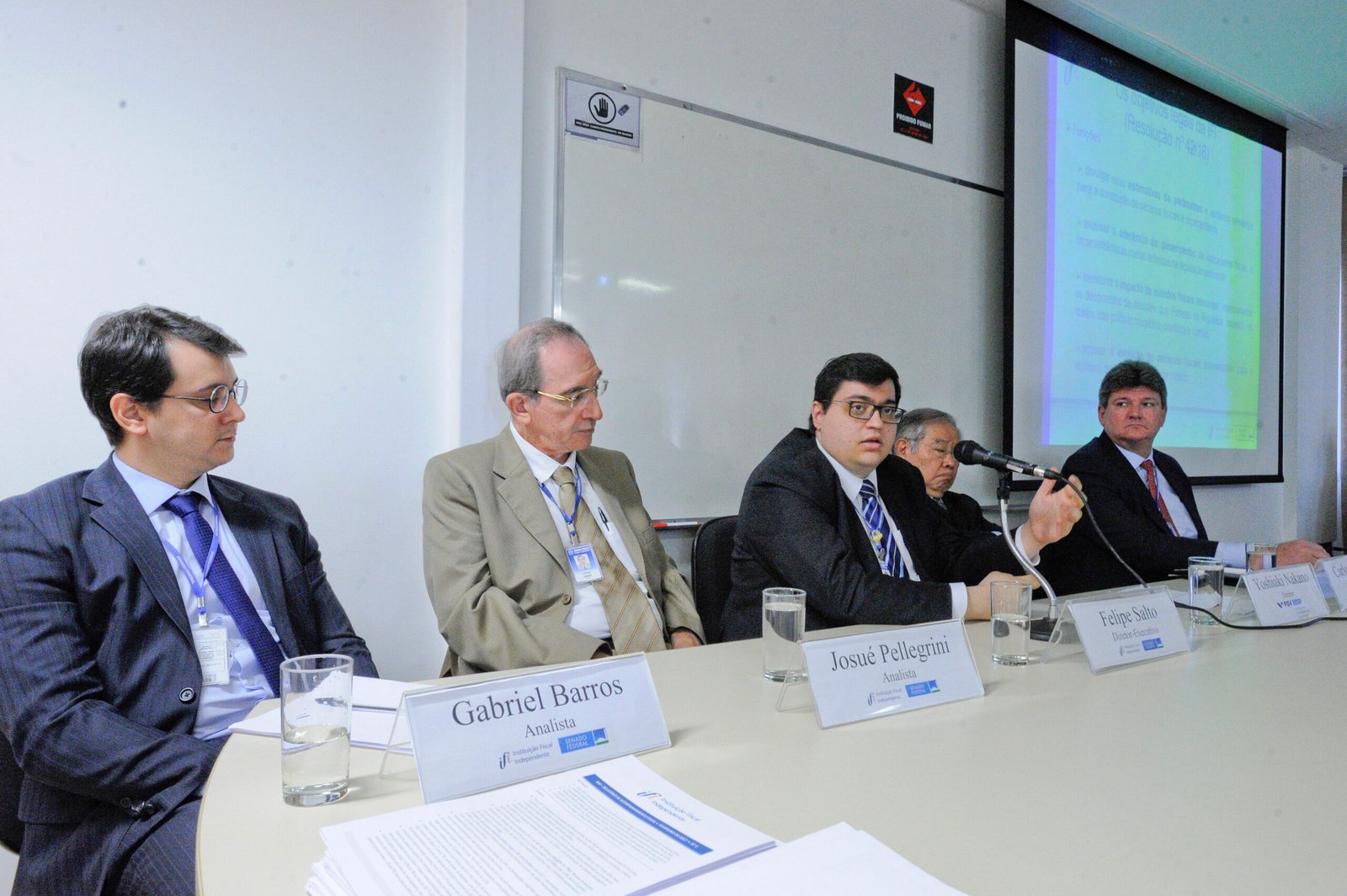 Analistas e diretor da Instituição Fiscal Independente sentados à mesa durante reunião, com apresentação projetada ao fundo