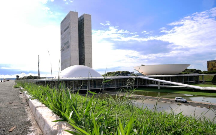 Torres e cúpulas do Congresso Nacional vistas da Esplanada dos Ministérios, com gramado em primeiro plano e céu parcialmente nublado