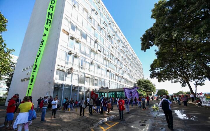 Fachada do prédio do Ministério da Fazenda, em Brasília, com manifestantes e uma faixa vertical durante protesto em 2017