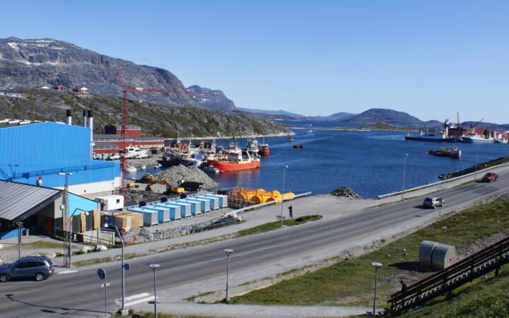 Porto de Nuuk, na Groenlândia, com navios, galpões e montanhas ao fundo