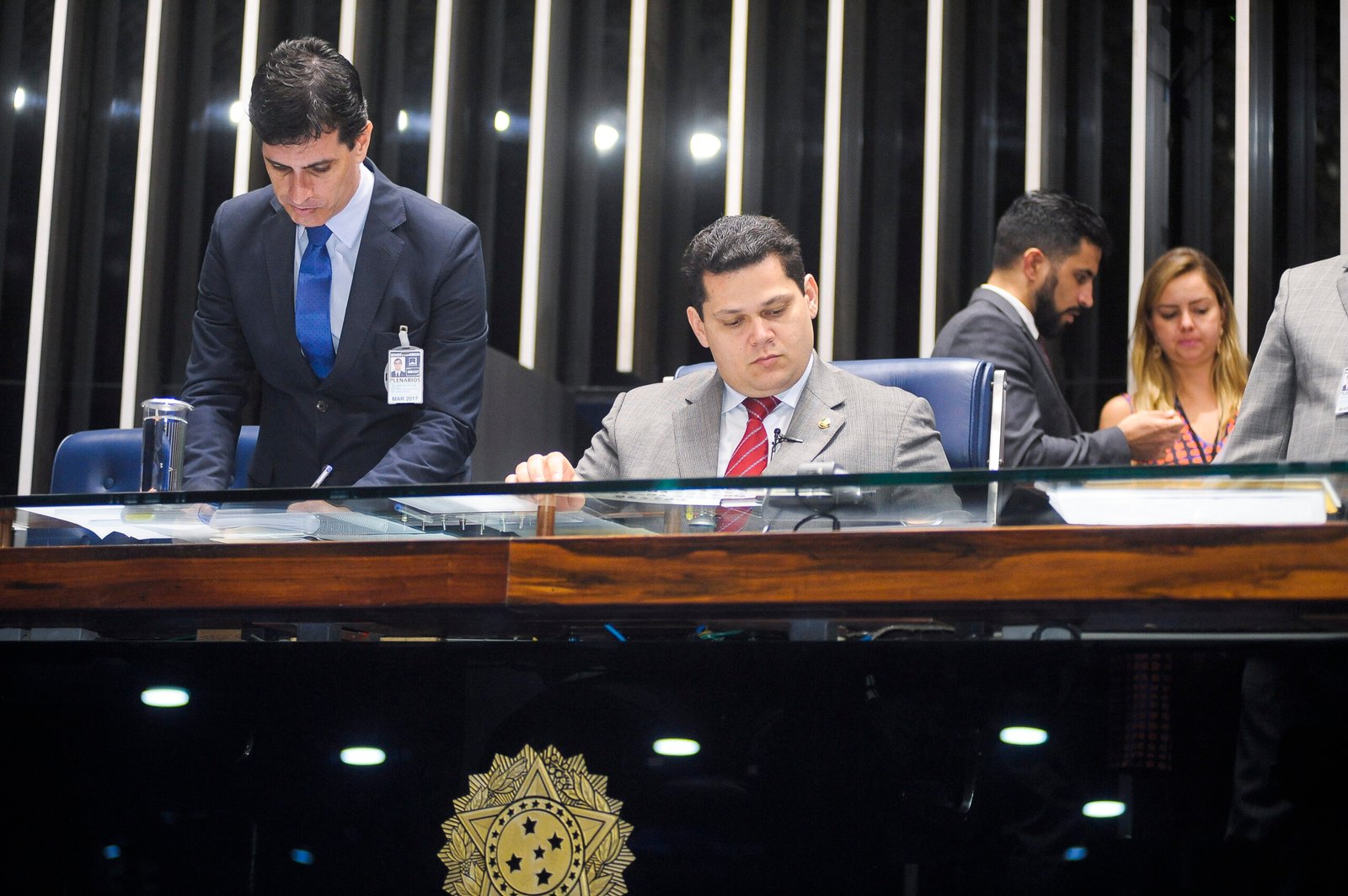 Davi Alcolumbre sentado à mesa diretora do Plenário do Senado, com assessores ao fundo e o brasão da República à frente