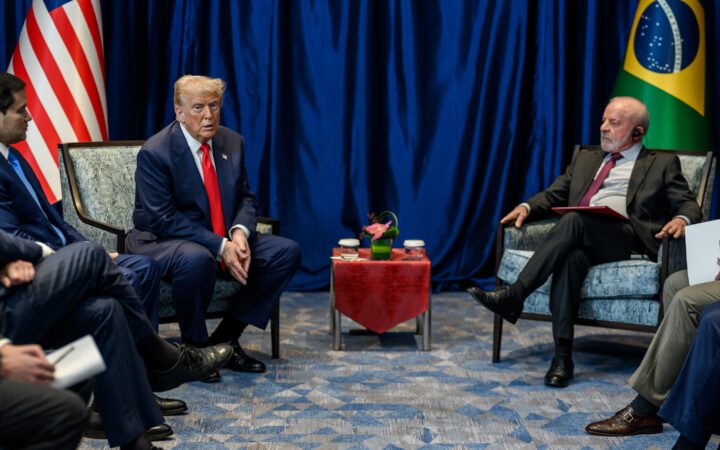 Donald Trump, sentado à esquerda, e Lula, sentado à direita, durante reunião bilateral com bandeiras dos Estados Unidos e do Brasil ao fundo