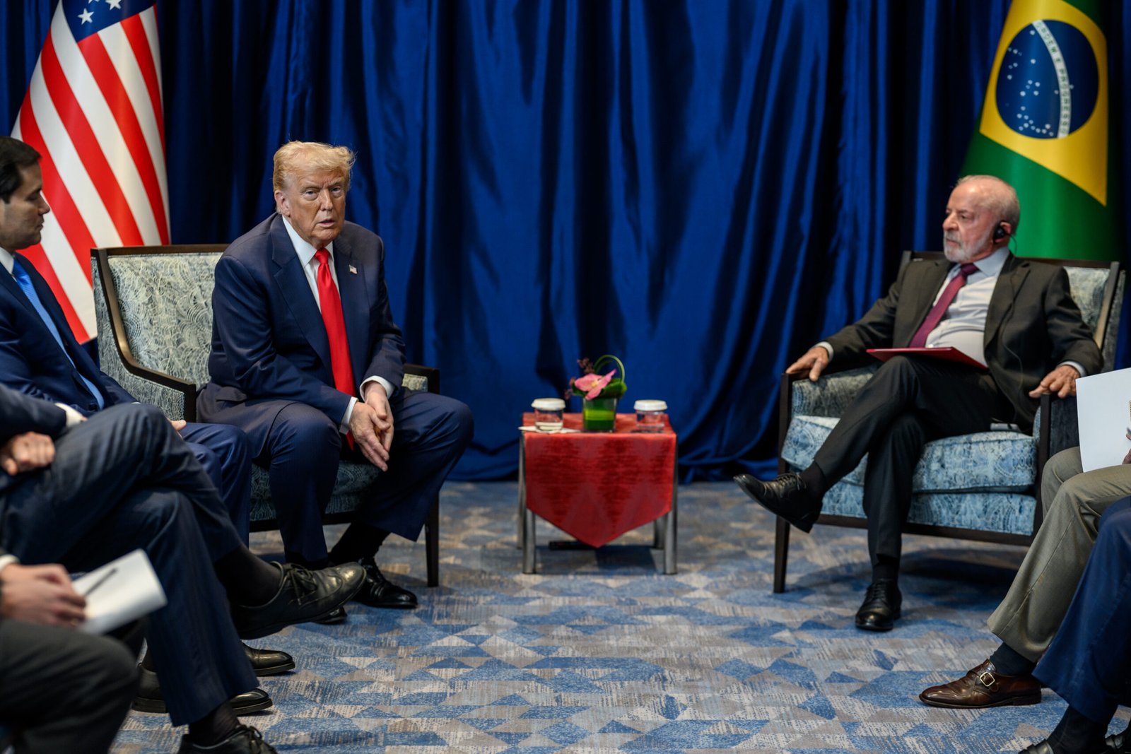 Donald Trump, sentado à esquerda, e Lula, sentado à direita, durante reunião bilateral com bandeiras dos Estados Unidos e do Brasil ao fundo