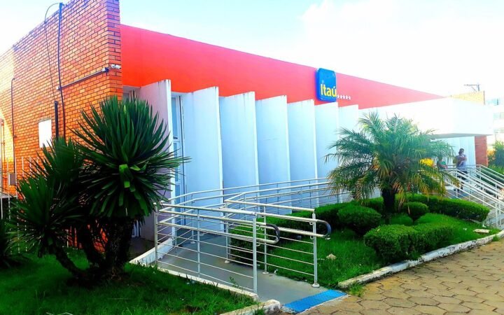 Fachada de uma agência do Itaú, com o logotipo azul na parede laranja e rampa de acesso