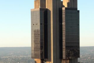 Torre da sede do Banco Central do Brasil em Brasília, de fachada escura, vista de cima sob céu azul.