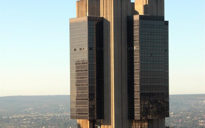 Torre da sede do Banco Central do Brasil em Brasília, de fachada escura, vista de cima sob céu azul.