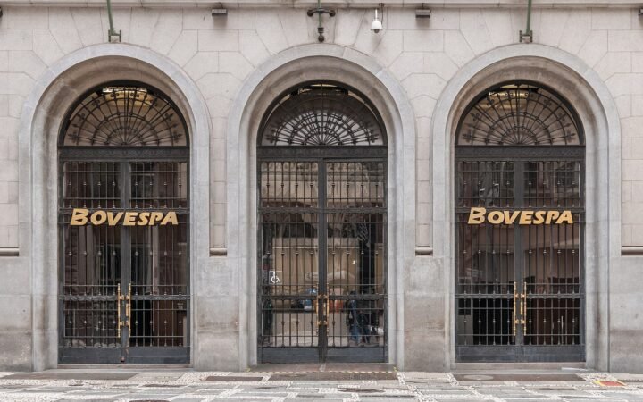 Três portas em arco, com grades de ferro, na fachada de pedra da antiga Bovespa, com o nome Bovespa em letras douradas