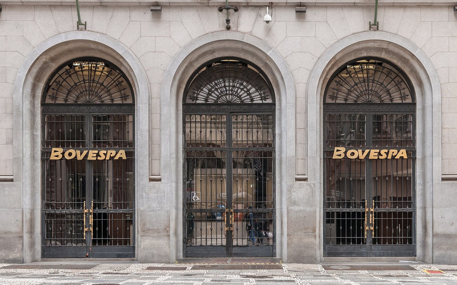 Três portas em arco, com grades de ferro, na fachada de pedra da antiga Bovespa, com o nome Bovespa em letras douradas