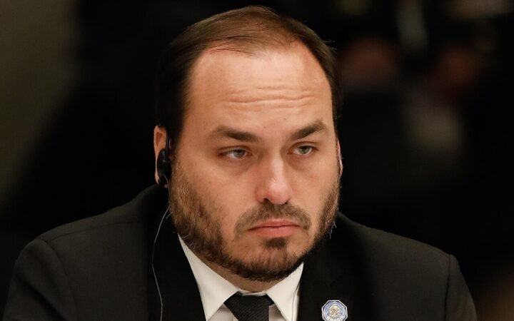 Carlos Bolsonaro, de terno escuro e fone de tradução, sentado a uma mesa durante encontro empresarial em Moscou, em 2022