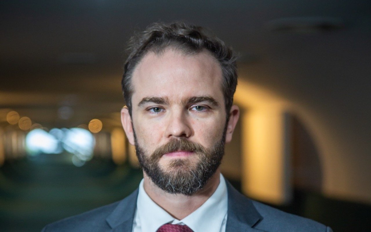 Retrato de Dario Durigan, de terno cinza e gravata vinho, em corredor do Ministério da Fazenda