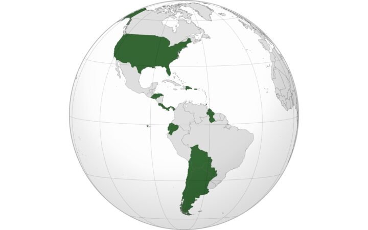 Mapa-múndi em projeção ortográfica centrado nas Américas, com Estados Unidos, Argentina, Chile, Bolívia, Paraguai, Equador, Honduras, Costa Rica, Panamá, República Dominicana e Guiana destacados em verde escuro e os demais países em cinza claro.