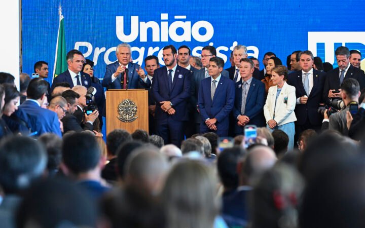 Lideranças de União Brasil e PP reunidas em um palco diante de painel azul com o nome União Progressista, no Salão Negro do Congresso.