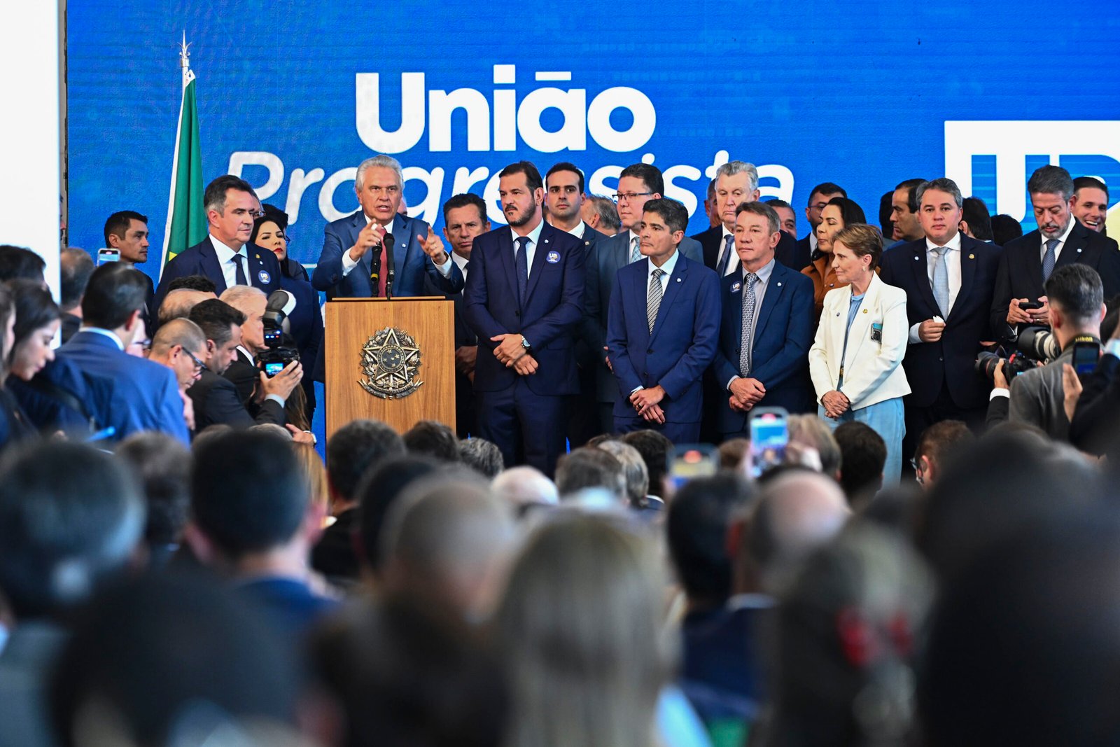 Lideranças de União Brasil e PP reunidas em um palco diante de painel azul com o nome União Progressista, no Salão Negro do Congresso.