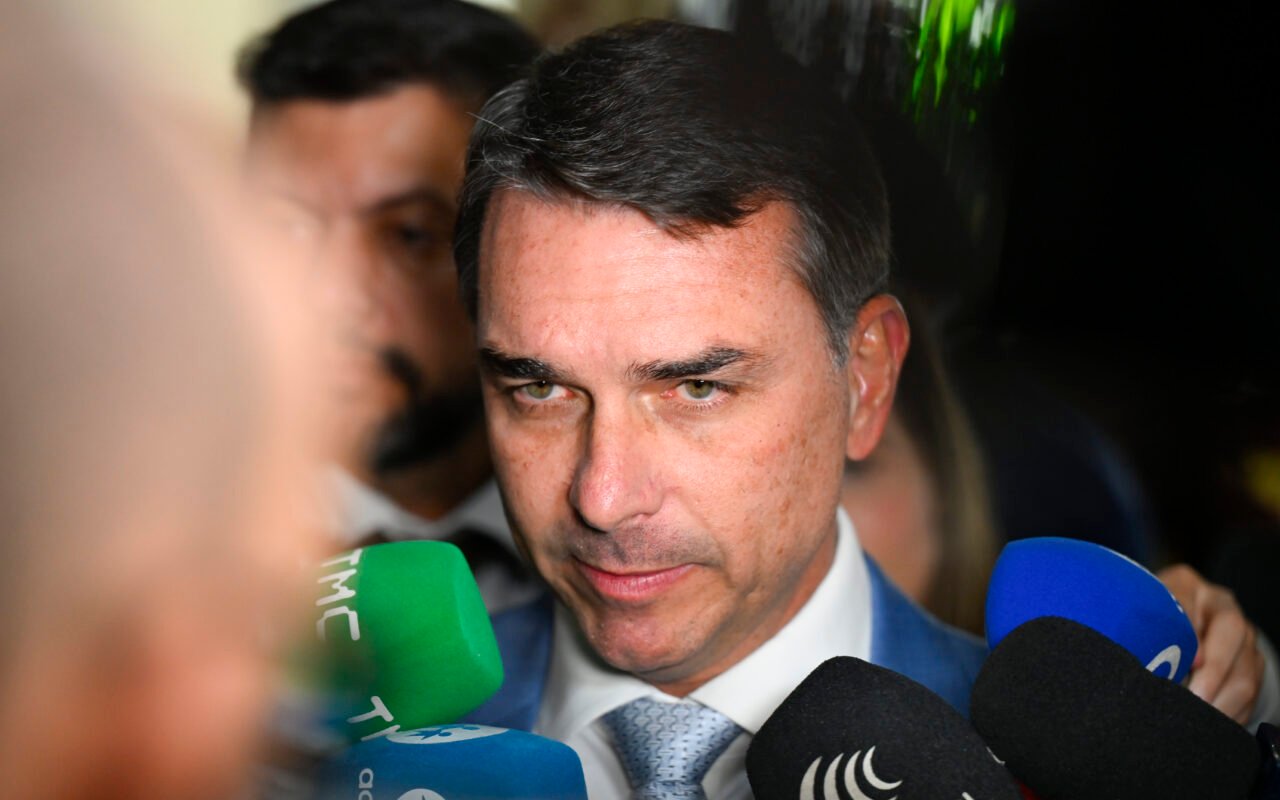 O senador Flávio Bolsonaro cercado por microfones durante entrevista no Senado Federal.