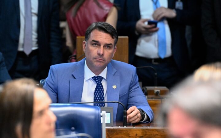 O senador Flávio Bolsonaro, de terno azul, sentado à bancada no Plenário do Senado.