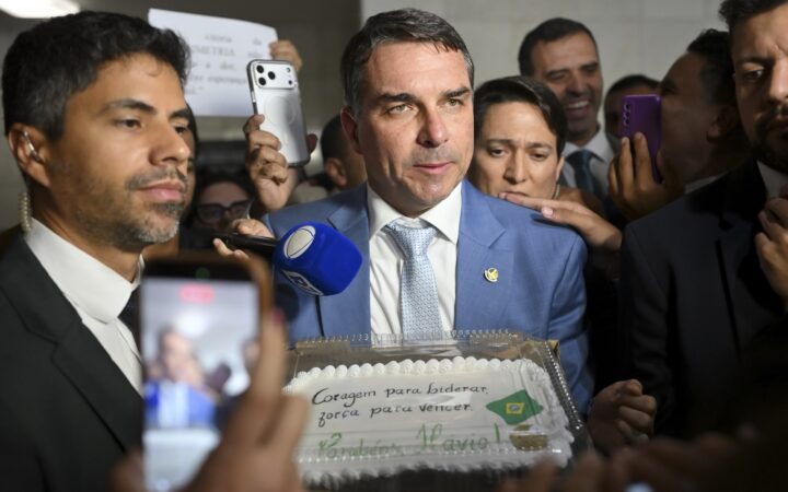 O senador Flávio Bolsonaro, de terno azul, cercado por repórteres e assessores durante entrevista no Senado