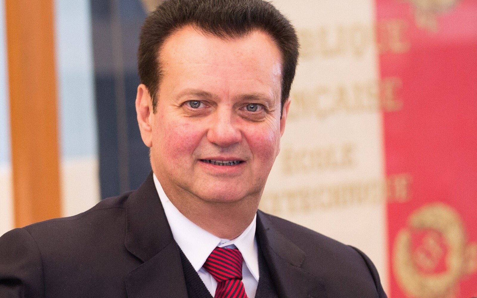 Retrato de Gilberto Kassab, de terno escuro e gravata vermelha, sorrindo