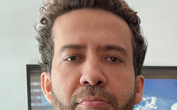 Retrato em close do deputado federal André Janones, de cabelo cacheado e barba, olhando para a câmera