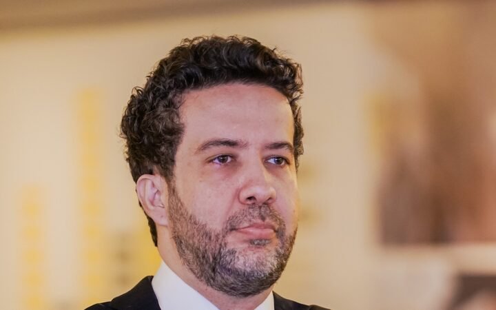 Retrato do deputado federal André Janones, de terno escuro e gravata, braços cruzados
