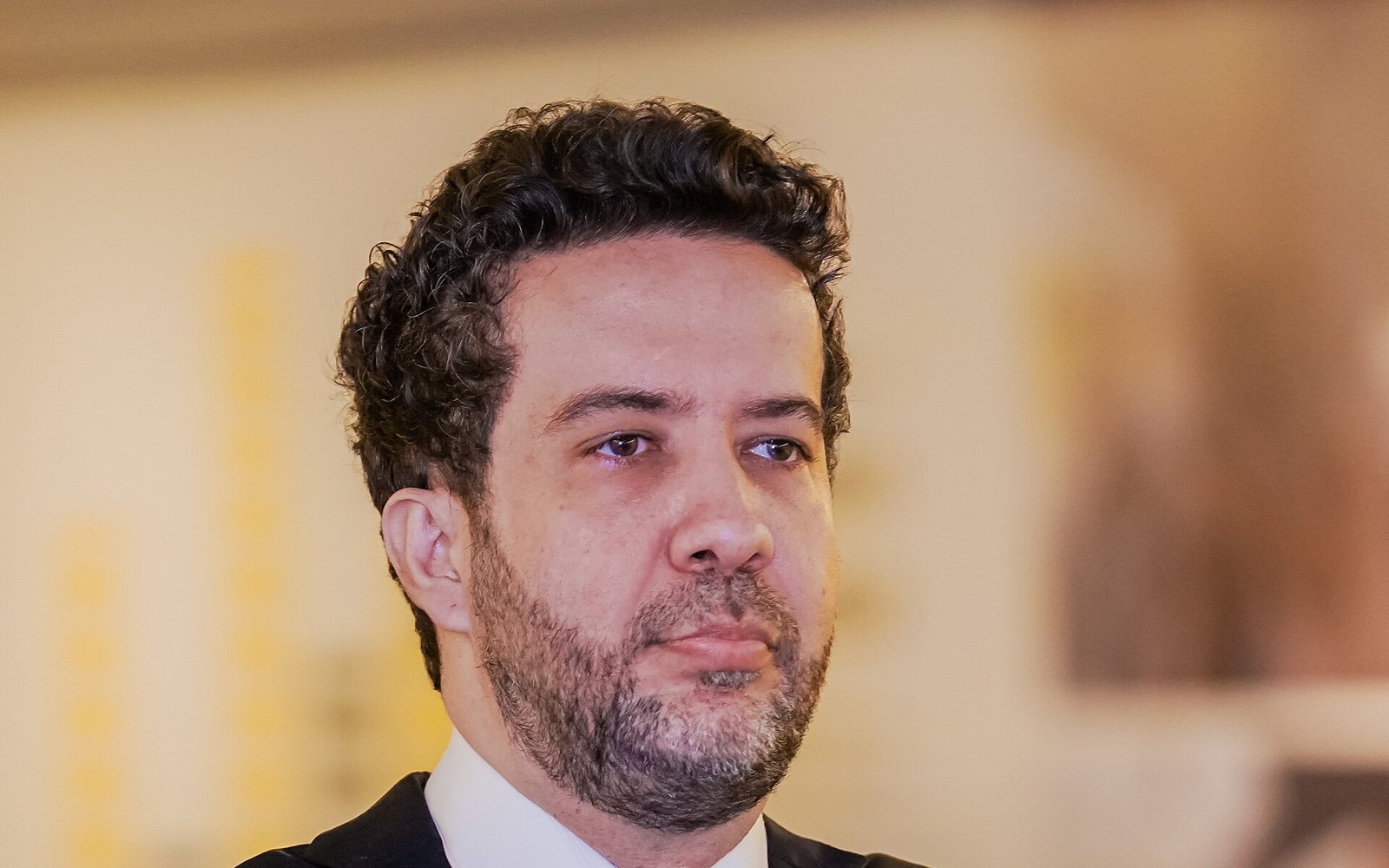 Retrato do deputado federal André Janones, de terno escuro e gravata, braços cruzados