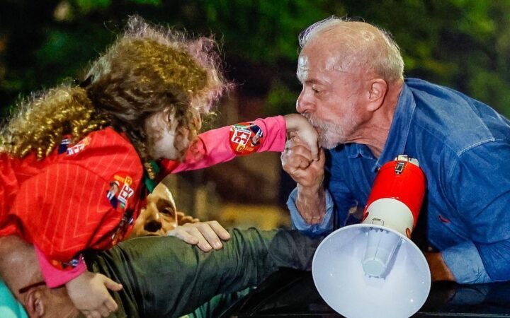 O presidente Lula, de camisa jeans e com um megafone, beija a mão de uma criança em ato de comemoração