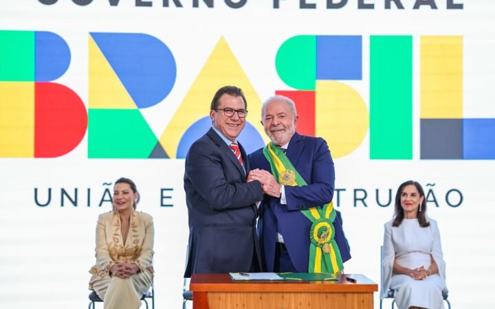 Luiz Marinho, de terno e gravata vermelha, aperta a mão do presidente Lula, de faixa presidencial, durante a posse do ministro do Trabalho, em Brasília