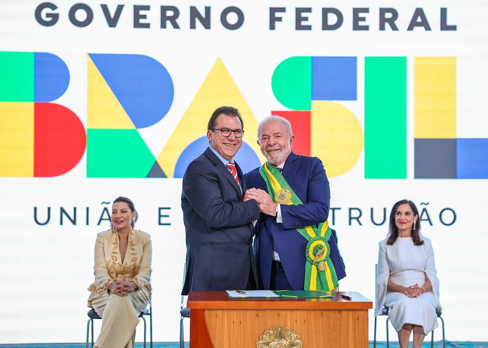 Luiz Marinho, de terno e gravata vermelha, aperta a mão do presidente Lula, de faixa presidencial, durante a posse do ministro do Trabalho, em Brasília
