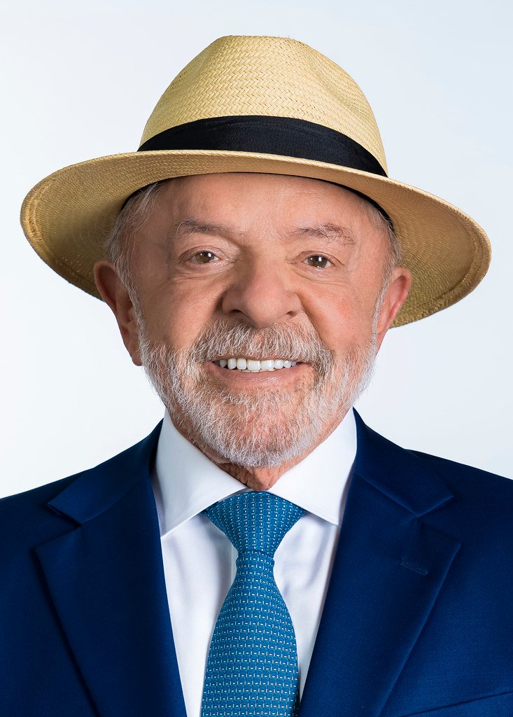 Lula sorri em retrato com chapéu de palha, terno azul e gravata azul.