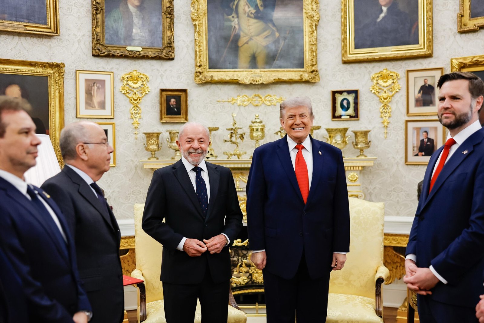 Lula e Donald Trump lado a lado, sorrindo, no Salão Oval da Casa Branca, com o vice J.D. Vance e outros presentes ao redor.