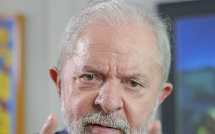 Retrato de Luiz Inácio Lula da Silva, de terno azul-escuro e gravata vermelha, gesticulando com os dois indicadores levantados durante entrevista.