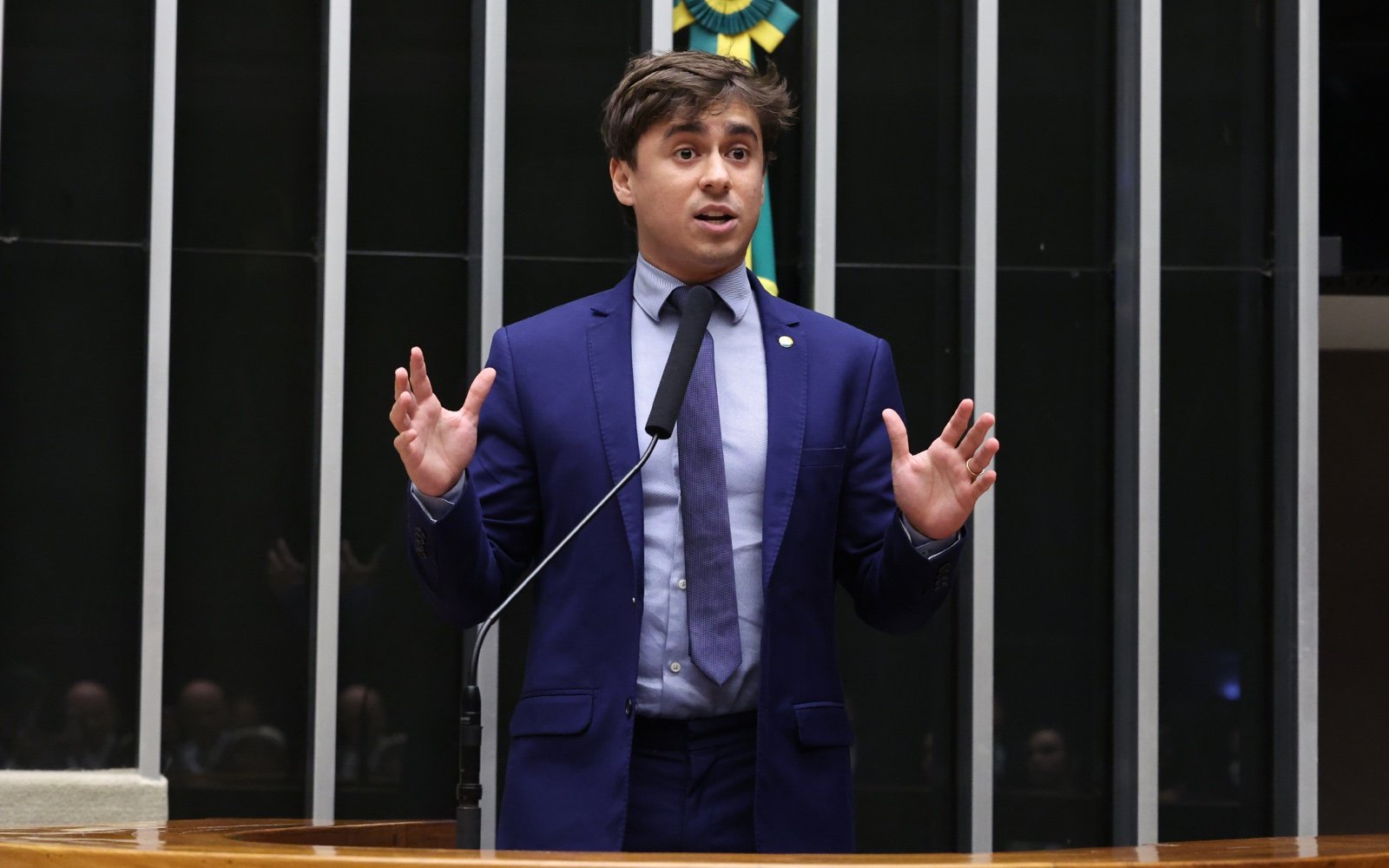 O deputado Nikolas Ferreira, de terno azul, discursa na tribuna do Plenário da Câmara com as mãos abertas