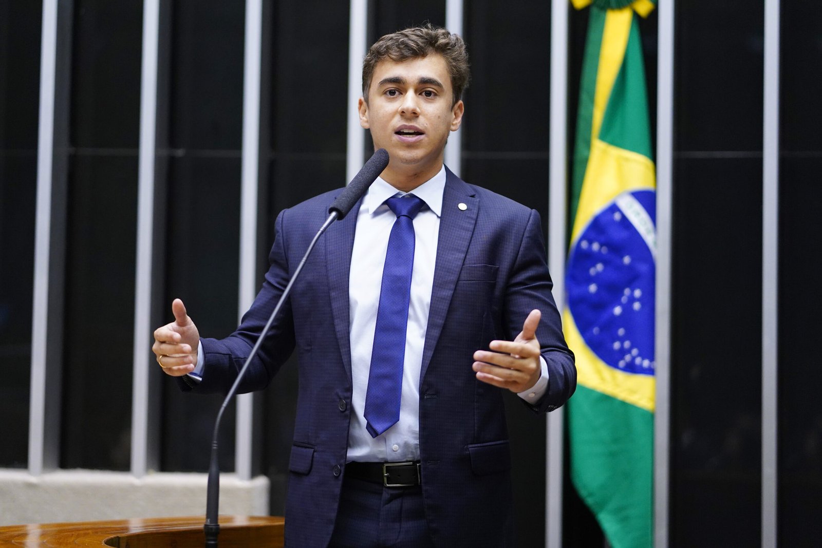 Deputado Nikolas Ferreira discursando na tribuna do plenário da Câmara, ao lado da bandeira do Brasil