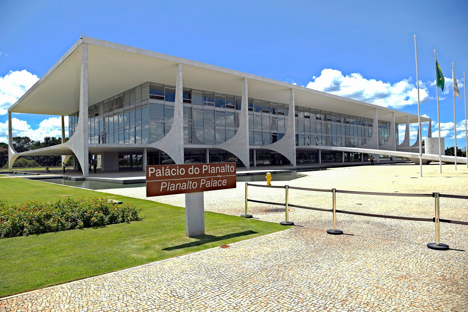 Fachada do Palácio do Planalto, com colunas brancas curvas e placa com o nome do prédio no gramado.