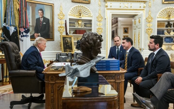 Donald Trump atrás da mesa do Salão Oval, diante de Eduardo Bolsonaro, Flávio Bolsonaro e Paulo Figueiredo sentados