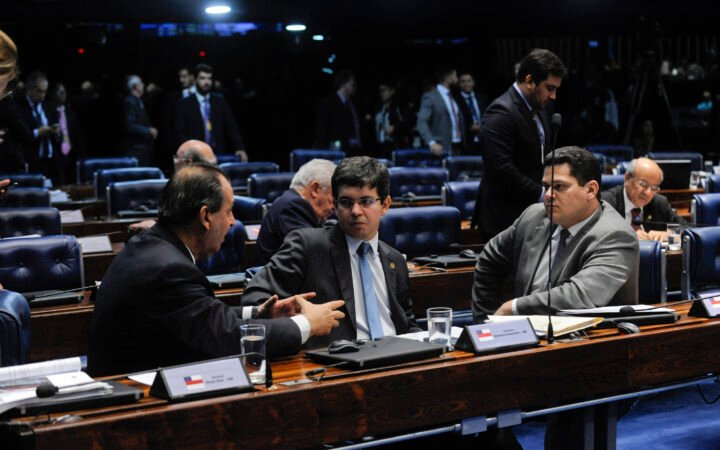 Senadores conversam em suas bancadas no plenário do Senado; à esquerda, Omar Aziz