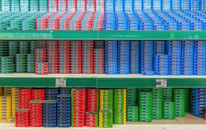 Prateleiras de supermercado com fileiras de latas de sardinha vermelhas, azuis, verdes e amarelas