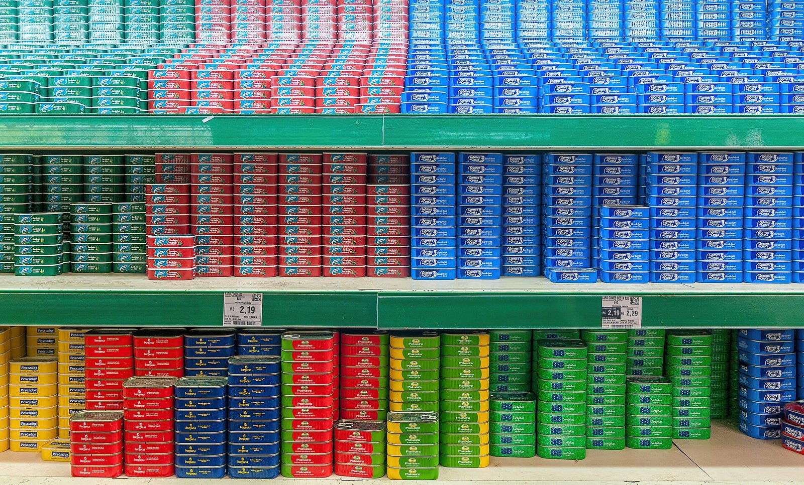 Prateleiras de supermercado com fileiras de latas de sardinha vermelhas, azuis, verdes e amarelas
